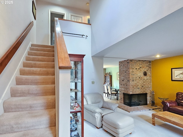 stairs with carpet floors, a high ceiling, and a brick fireplace