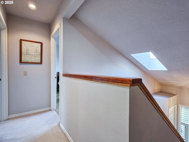 hall with vaulted ceiling with skylight, carpet, baseboards, and a textured ceiling