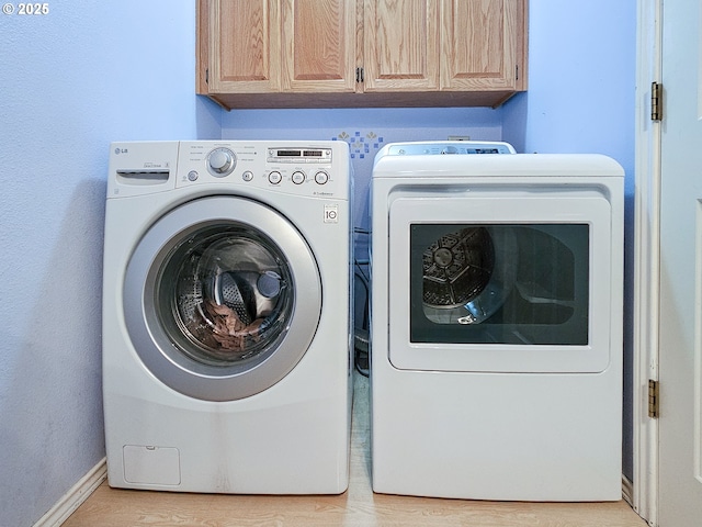 laundry room with light wood-type flooring, cabinet space, washer and clothes dryer, and baseboards