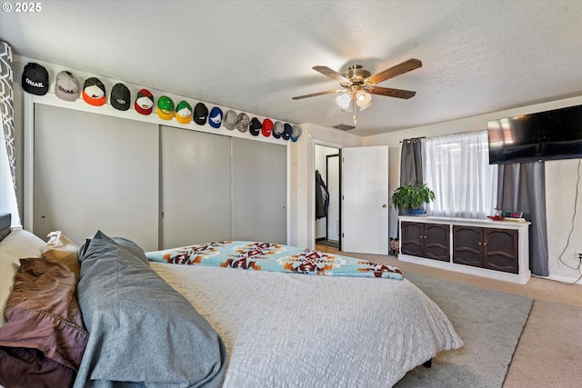 bedroom featuring a closet, ceiling fan, visible vents, a textured ceiling, and carpet floors