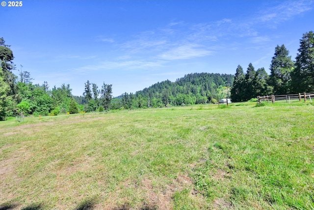 view of yard with a view of trees, fence, and a rural view