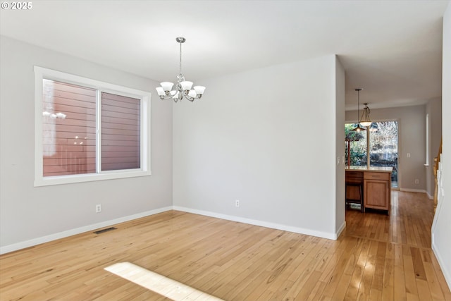spare room featuring light wood-type flooring, baseboards, a chandelier, and visible vents
