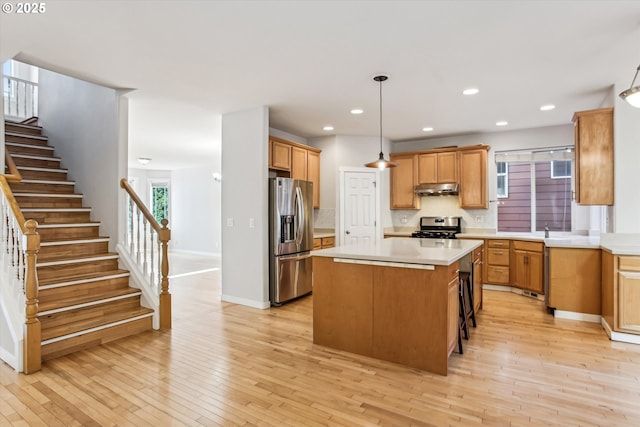 kitchen featuring light countertops, a kitchen island, stainless steel appliances, and under cabinet range hood
