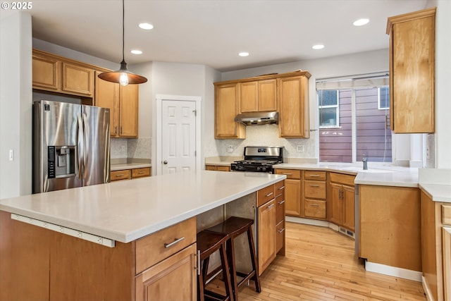 kitchen featuring a center island, under cabinet range hood, a sink, backsplash, and stainless steel appliances