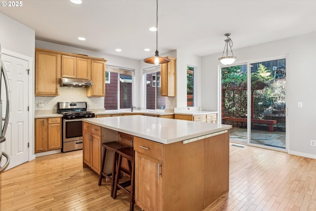 kitchen featuring a kitchen island, stainless steel range with gas cooktop, light countertops, light wood-type flooring, and under cabinet range hood