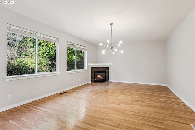unfurnished living room featuring visible vents, a tiled fireplace, baseboards, a notable chandelier, and light wood-style floors