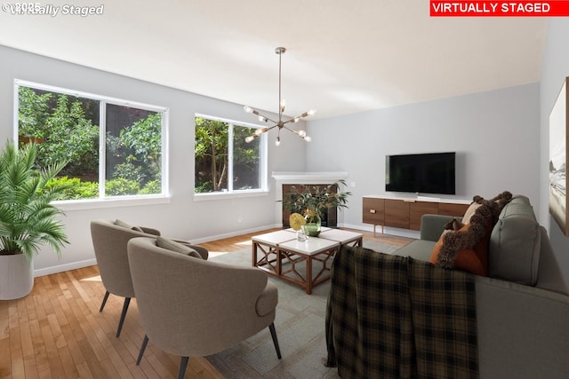 living area featuring baseboards, light wood-style floors, a notable chandelier, and a healthy amount of sunlight