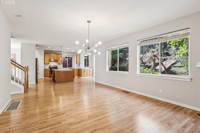 unfurnished living room featuring a notable chandelier, baseboards, light wood-type flooring, visible vents, and stairway