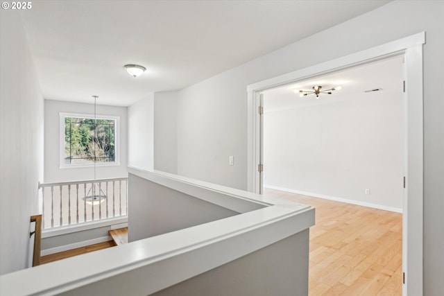 corridor with baseboards, a notable chandelier, and light wood finished floors
