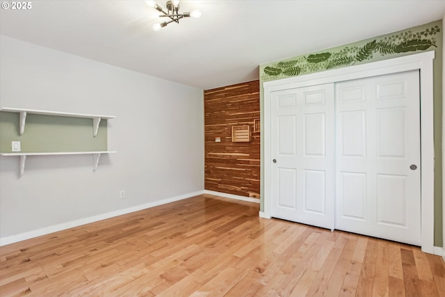 unfurnished bedroom with a chandelier, wood walls, light wood-style flooring, baseboards, and a closet