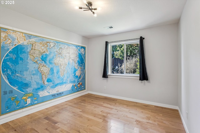 unfurnished room featuring baseboards, visible vents, and wood finished floors