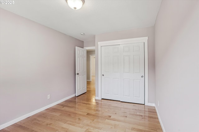 unfurnished bedroom featuring light wood-type flooring, baseboards, and a closet