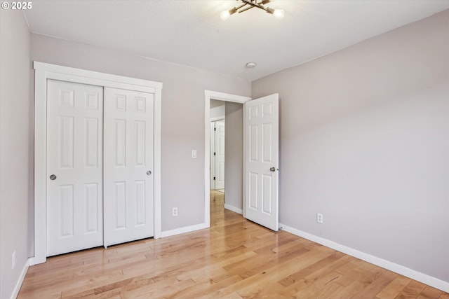 unfurnished bedroom with baseboards, a closet, light wood-type flooring, and a notable chandelier