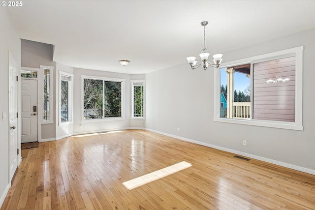 empty room featuring baseboards, a notable chandelier, hardwood / wood-style flooring, and visible vents