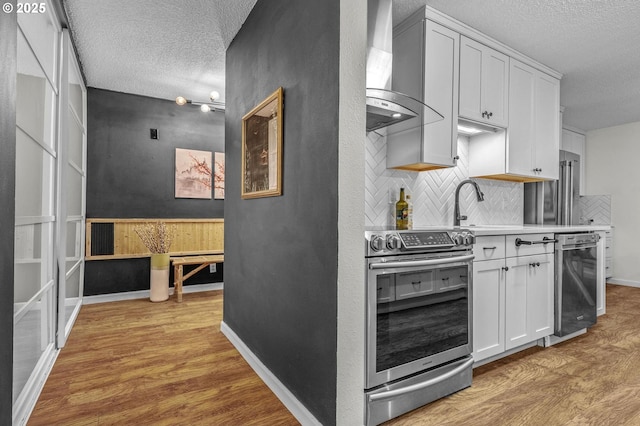 2393 SW Park Pl Unit 113, Portland, OR 97205 - kitchen with appliances with stainless steel finishes, wall chimney range hood, light wood-style flooring, a textured ceiling, and tasteful backsplash
