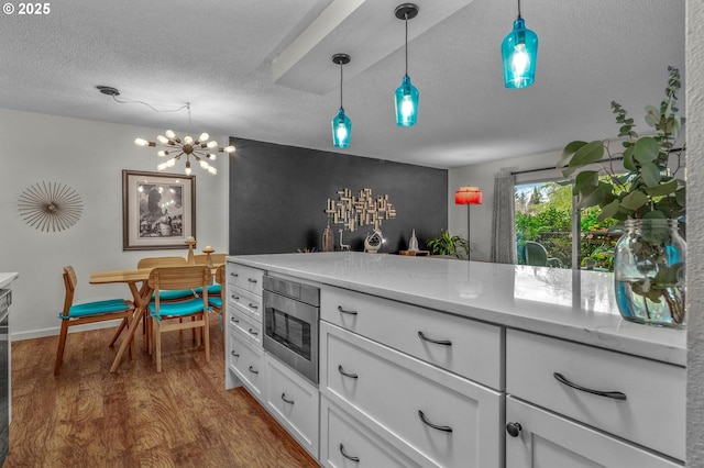 2393 SW Park Pl Unit 113, Portland, OR 97205 - kitchen featuring stainless steel microwave, a textured ceiling, dark wood-style floors, white cabinetry, and decorative light fixtures