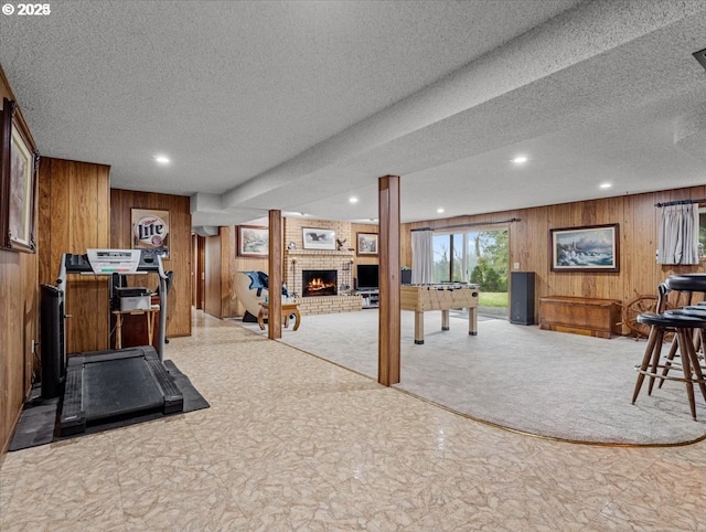 workout area with a textured ceiling, wooden walls, a brick fireplace, and recessed lighting