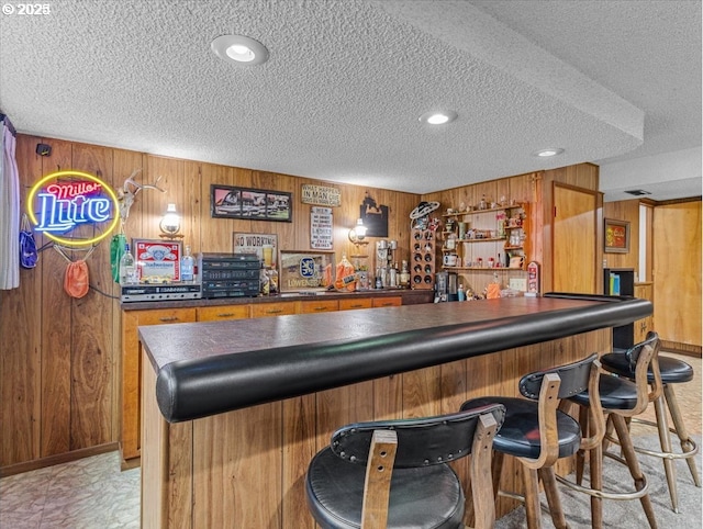 bar with wooden walls, a bar, and a textured ceiling