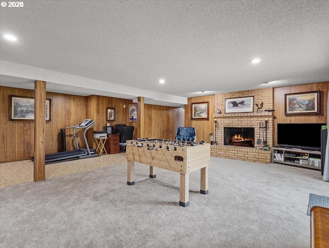 recreation room with a textured ceiling, recessed lighting, carpet floors, a brick fireplace, and wooden walls