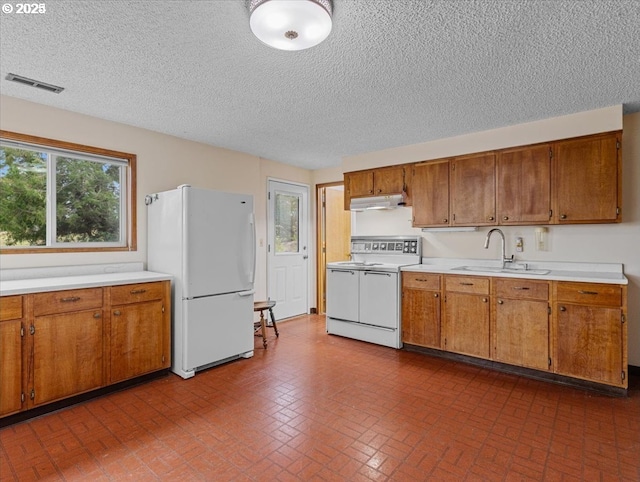 kitchen featuring white appliances, visible vents, under cabinet range hood, a sink, and brown cabinets