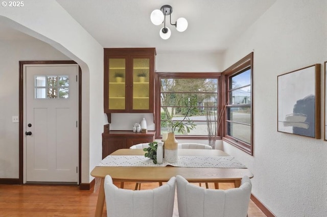 dining room featuring arched walkways, plenty of natural light, light wood finished floors, and baseboards