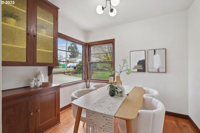 dining area featuring light wood-type flooring, baseboards, and a notable chandelier