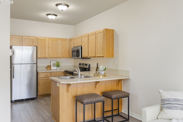 kitchen featuring light brown cabinets, a kitchen breakfast bar, stainless steel appliances, a peninsula, and light countertops