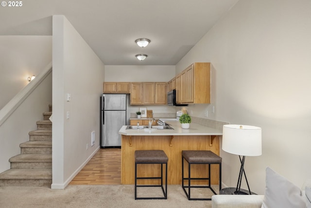 kitchen with a breakfast bar, a peninsula, freestanding refrigerator, a sink, and light countertops