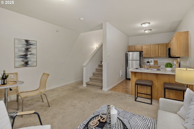 kitchen featuring a breakfast bar area, a peninsula, freestanding refrigerator, light countertops, and light carpet