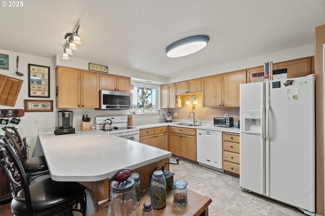 kitchen with white appliances, a breakfast bar area, kitchen peninsula, and a textured ceiling