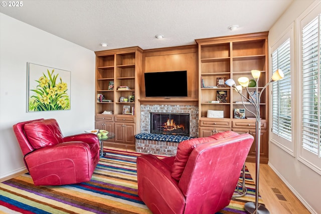 living area featuring a healthy amount of sunlight, a brick fireplace, light wood-type flooring, and a textured ceiling