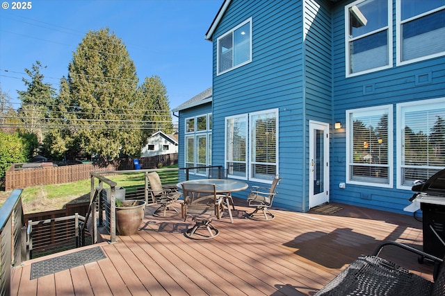 deck featuring outdoor dining area, fence, and a lawn