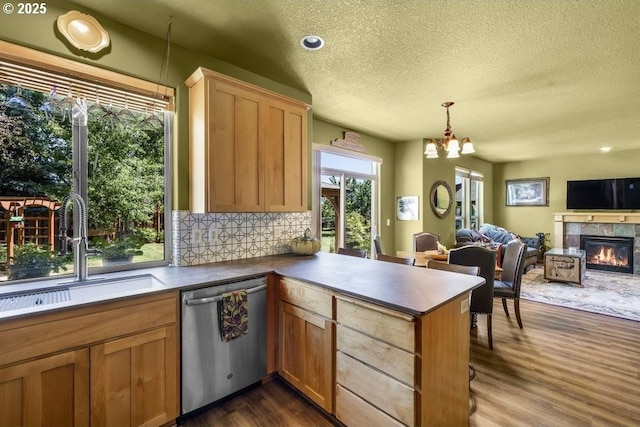 kitchen featuring a tiled fireplace, dark wood-type flooring, a sink, dishwasher, and a peninsula