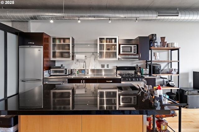 kitchen featuring a toaster, under cabinet range hood, stainless steel countertops, a kitchen island, and appliances with stainless steel finishes