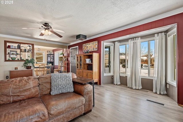 living room with ceiling fan, ornamental molding, a textured ceiling, and light hardwood / wood-style floors