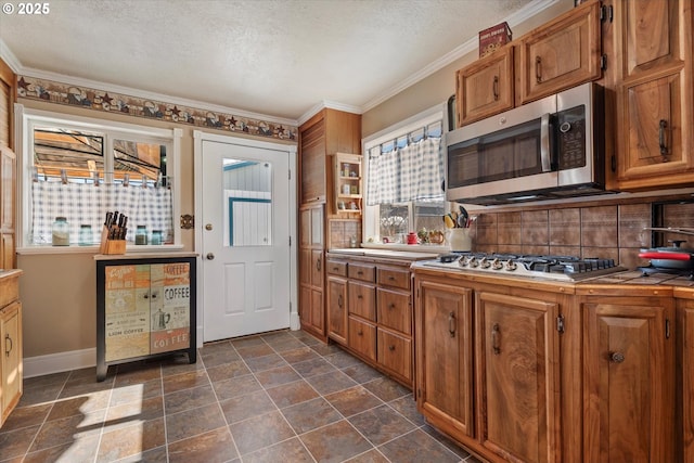 kitchen featuring tile counters, a textured ceiling, appliances with stainless steel finishes, crown molding, and decorative backsplash