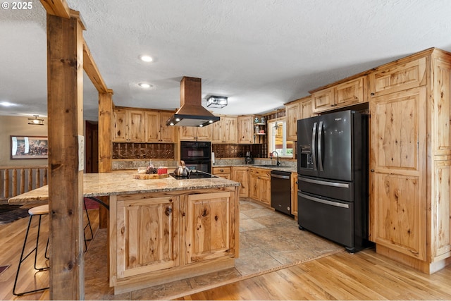 73594 Davis Ln, Pendleton, OR 97801 - kitchen featuring black appliances, island exhaust hood, light wood-style floors, light stone countertops, and a textured ceiling