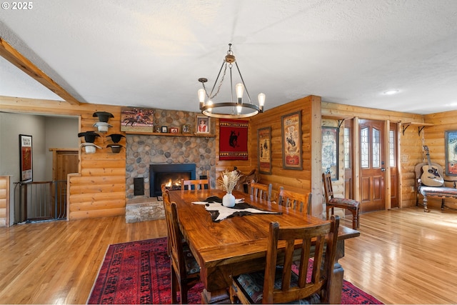 73594 Davis Ln, Pendleton, OR 97801 - dining space featuring log walls, light wood-style flooring, a stone fireplace, a chandelier, and a textured ceiling