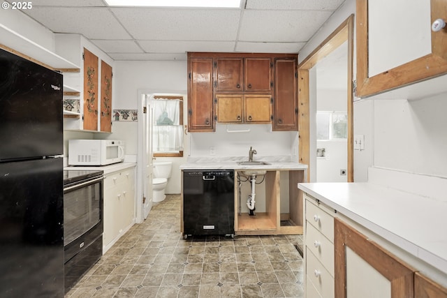 kitchen featuring brown cabinets, light countertops, a paneled ceiling, black appliances, and open shelves