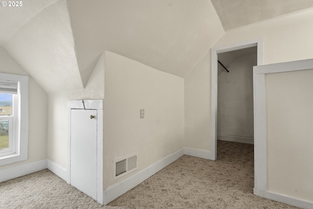 additional living space with a textured ceiling, lofted ceiling, light carpet, visible vents, and baseboards