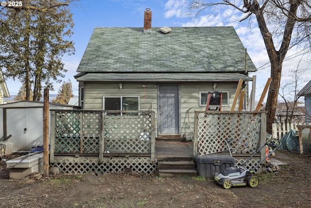 rear view of property featuring a chimney, a storage unit, and an outbuilding