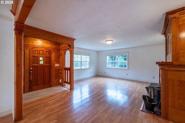 entrance foyer featuring ornamental molding, a wood stove, baseboards, and light wood finished floors