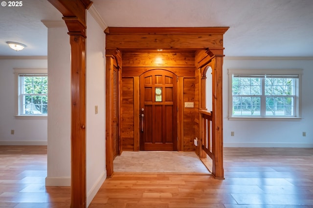 foyer featuring baseboards, ornamental molding, light wood-type flooring, and ornate columns