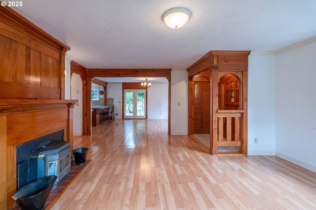 unfurnished living room featuring light wood-style flooring, baseboards, french doors, ornamental molding, and an inviting chandelier