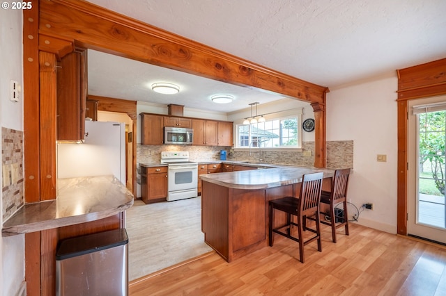 kitchen featuring white appliances, plenty of natural light, brown cabinets, a peninsula, and a sink