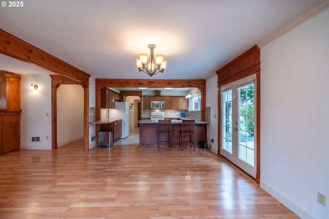 kitchen featuring tasteful backsplash, stainless steel microwave, brown cabinets, freestanding refrigerator, and a peninsula