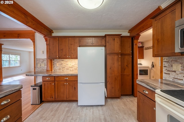 kitchen featuring light wood-style floors, backsplash, freestanding refrigerator, brown cabinetry, and washer / dryer