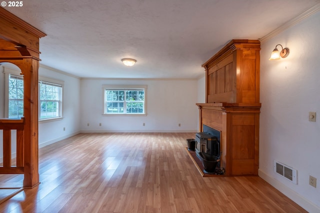 unfurnished living room with ornamental molding, light wood-type flooring, visible vents, and baseboards