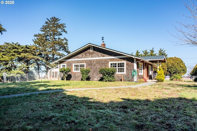 view of front facade featuring metal roof, a chimney, fence, and a front lawn