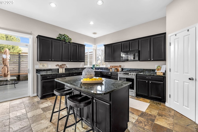 kitchen with a breakfast bar, pendant lighting, a kitchen island, dark stone counters, and black appliances